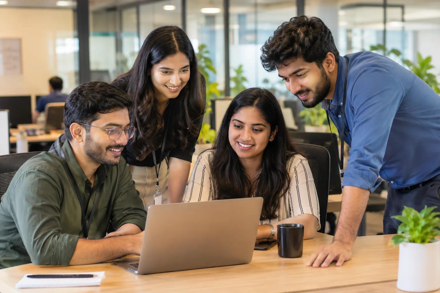 Four colleagues smiling around a laptop in a modern office